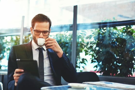 Man drinking coffee and looking at a tablet.